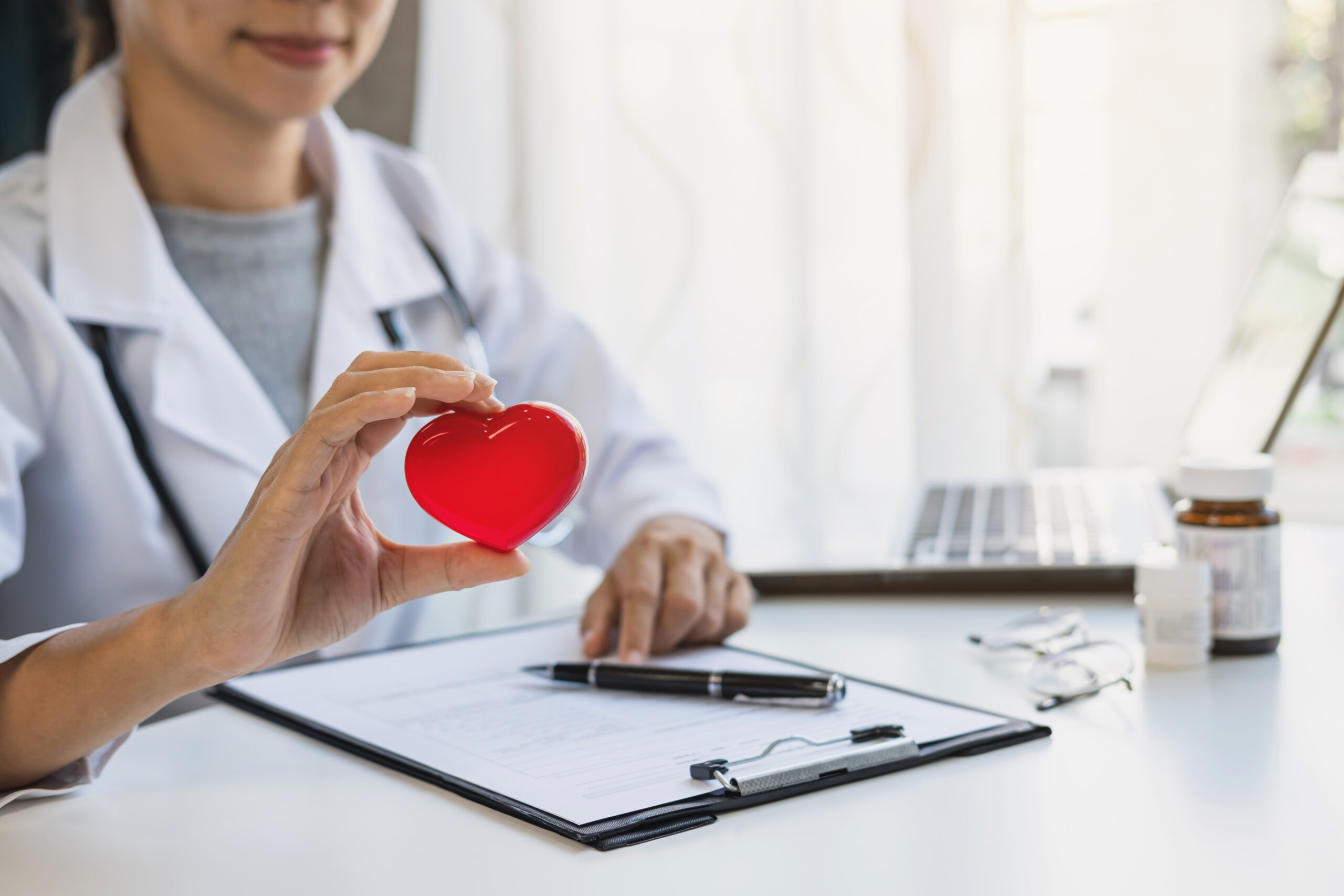 Young female doctor with the stethoscope holding red heart, cardiolog healthy care concept